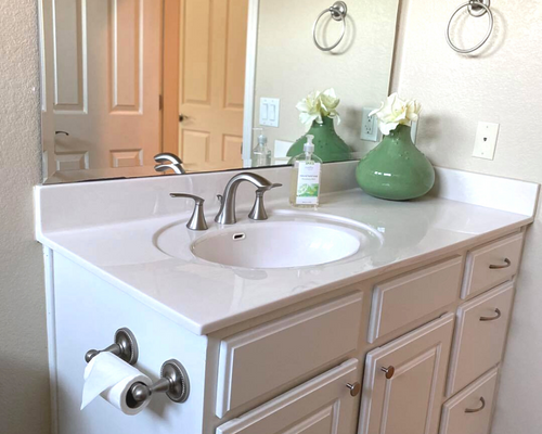 Bathroom vanity with white sink, chrome faucet, green vase, and wall mirror by an open door