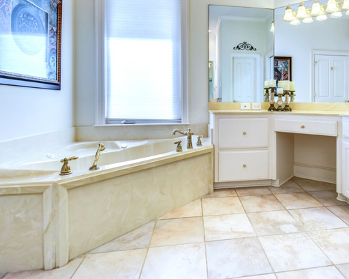 Bright bathroom with a marble bathtub, vanity, large mirror, and beige tile floor