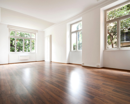 Bright empty room with hardwood floors and large windows letting in natural light