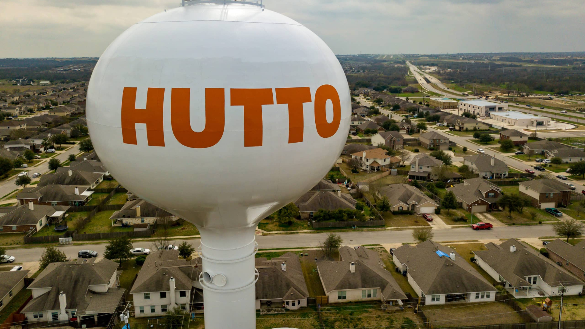 White water tower with orange “HUTTO” lettering above a suburban neighborhood