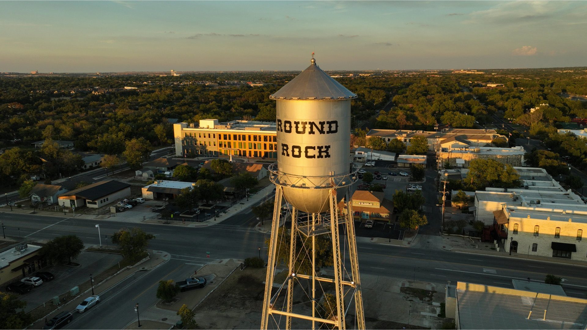 Sunset aerial view of a water tower labeled “ROUND ROCK” over a suburban cityscape