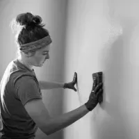 Person smoothing a white wall with a putty knife and sanding block