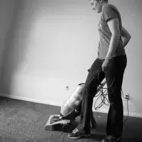 Person vacuuming carpet next to a standing vacuum cleaner in a bare room