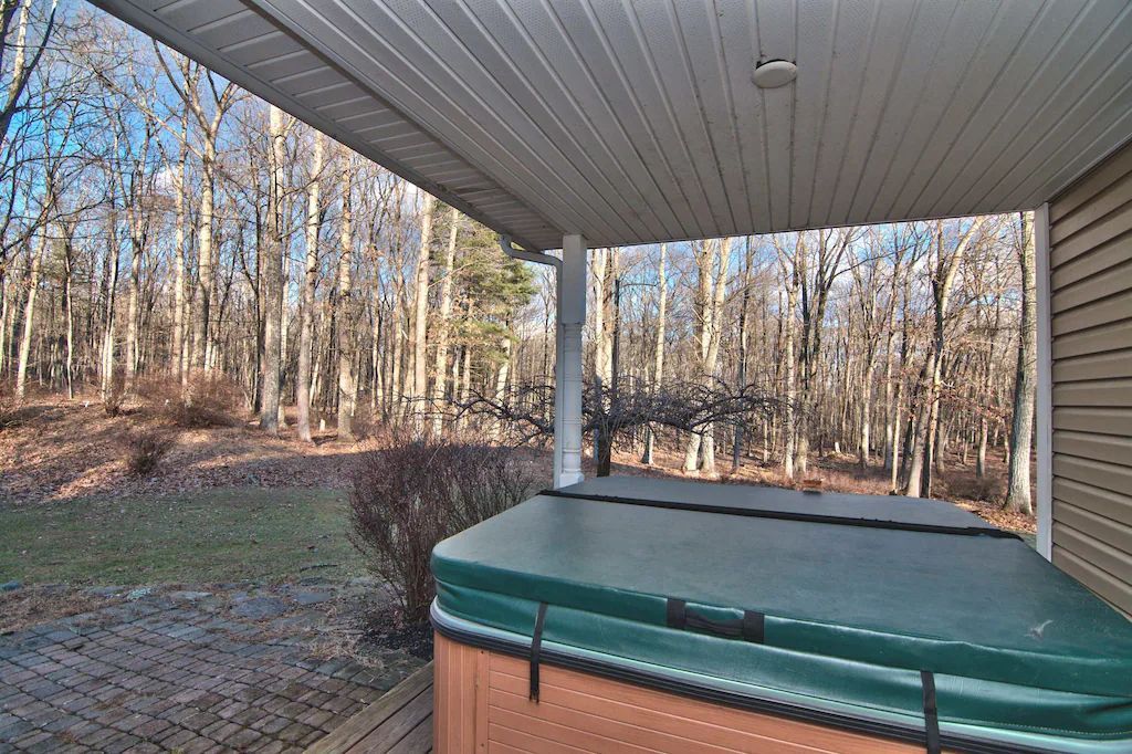 A hot tub with a green cover is under a porch with trees in the background