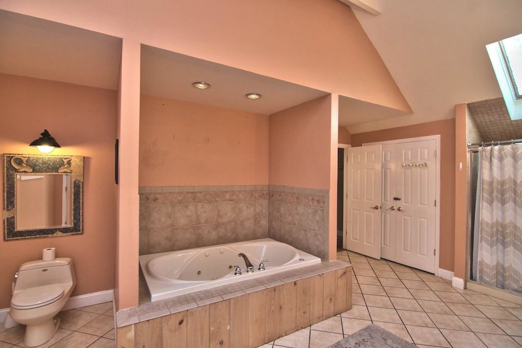 A bathroom with a jacuzzi tub , toilet , mirror and skylight.
