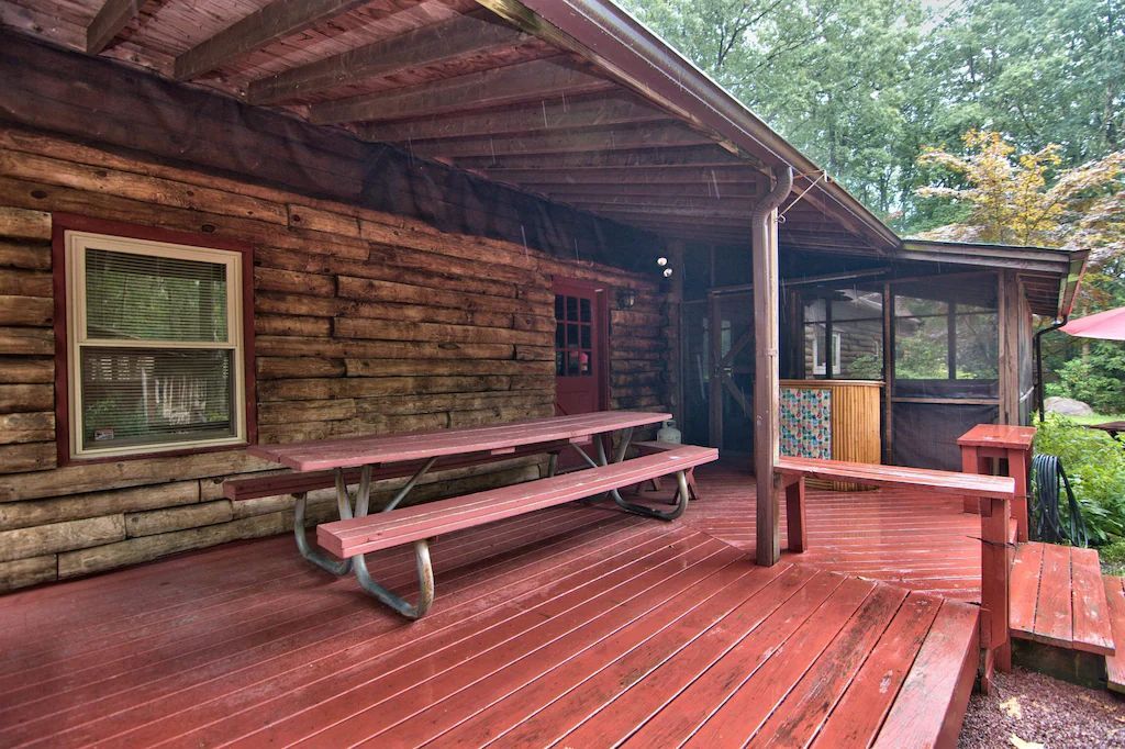 A wooden deck with a picnic table and benches in front of a log cabin.
