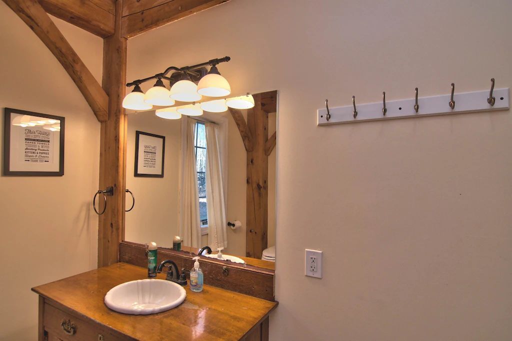 A bathroom with a sink , mirror and hooks on the wall.