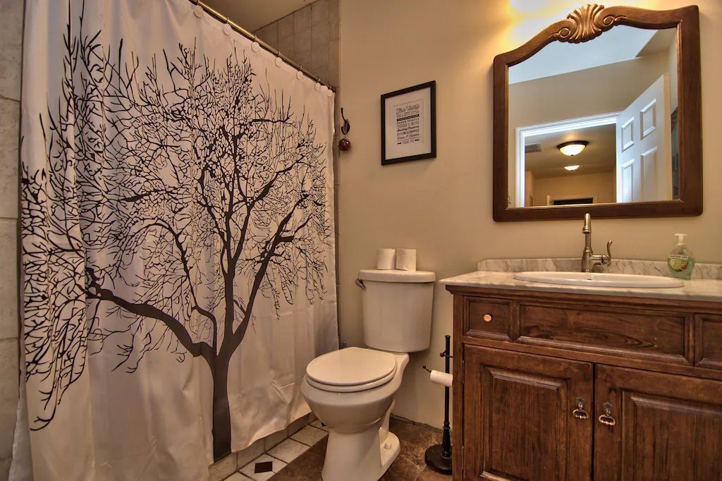 A bathroom with a toilet , sink , mirror and shower curtain with a tree on it.