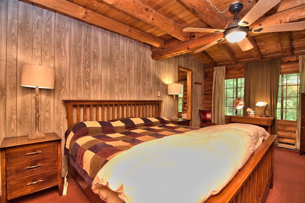 A bedroom in a log cabin with a king size bed and a ceiling fan.
