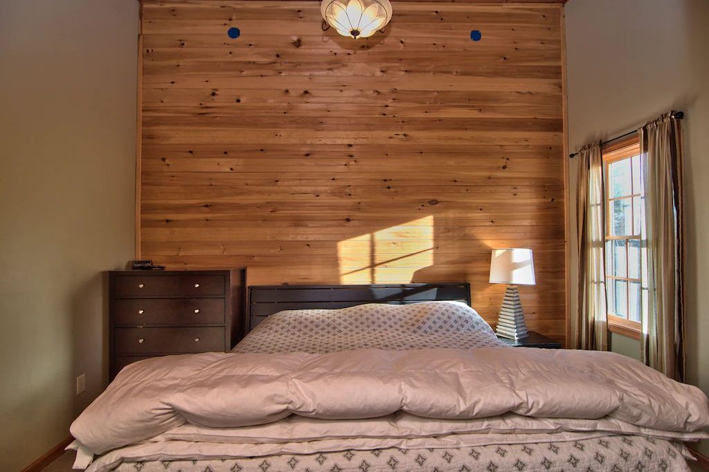 A bedroom with a bed , dresser , lamp and wooden walls.
