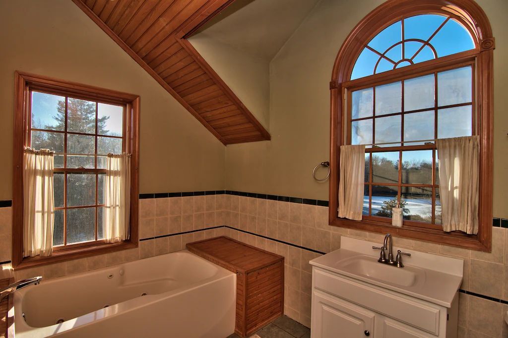 A bathroom with a tub , sink , and two windows.