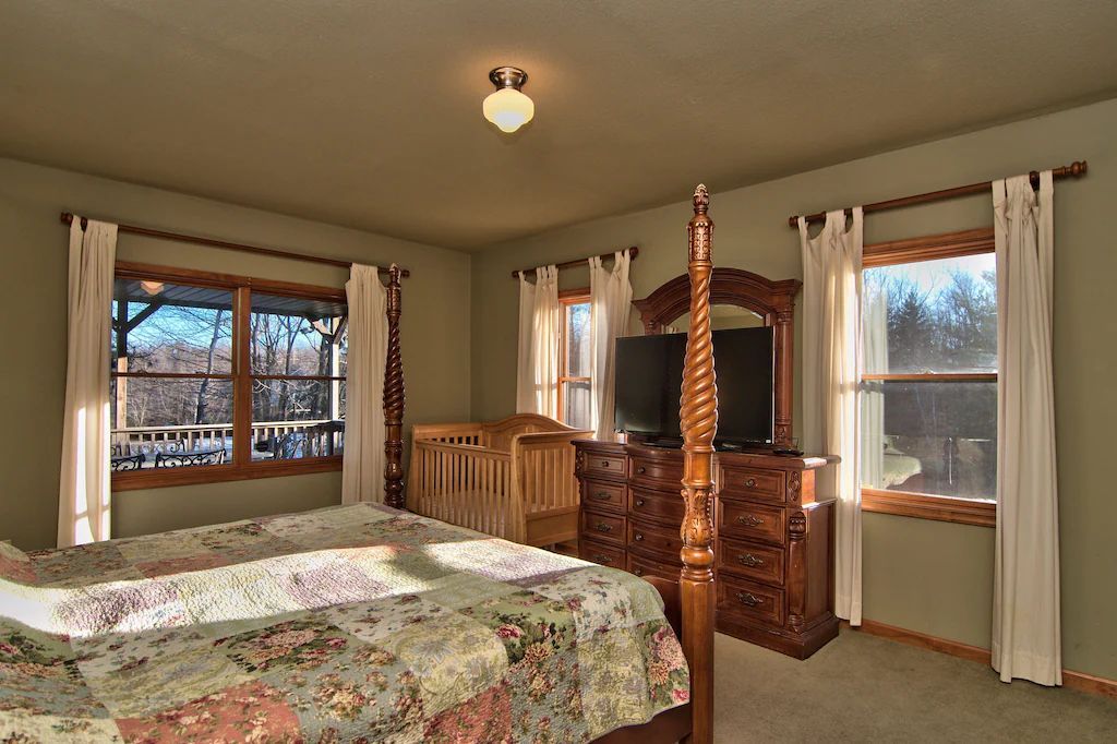 A bedroom with a four poster bed , dresser , and television.