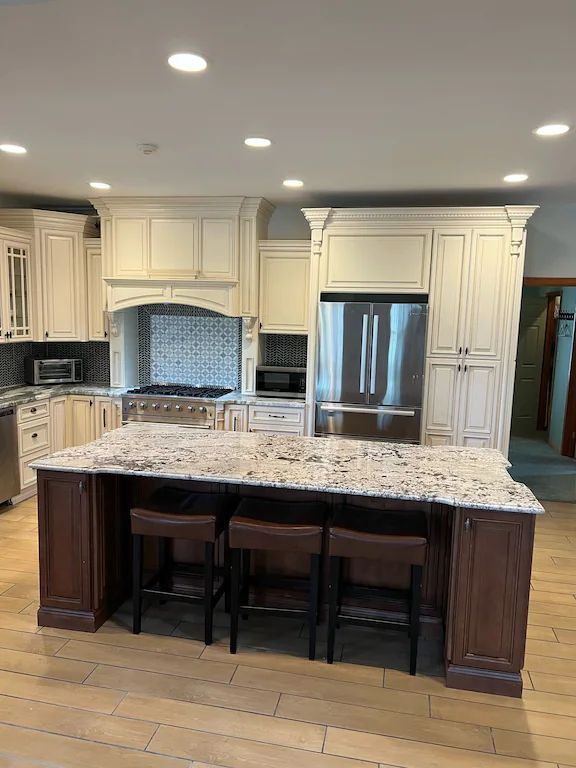 A kitchen with white cabinets , granite counter tops , stainless steel appliances and a large island.