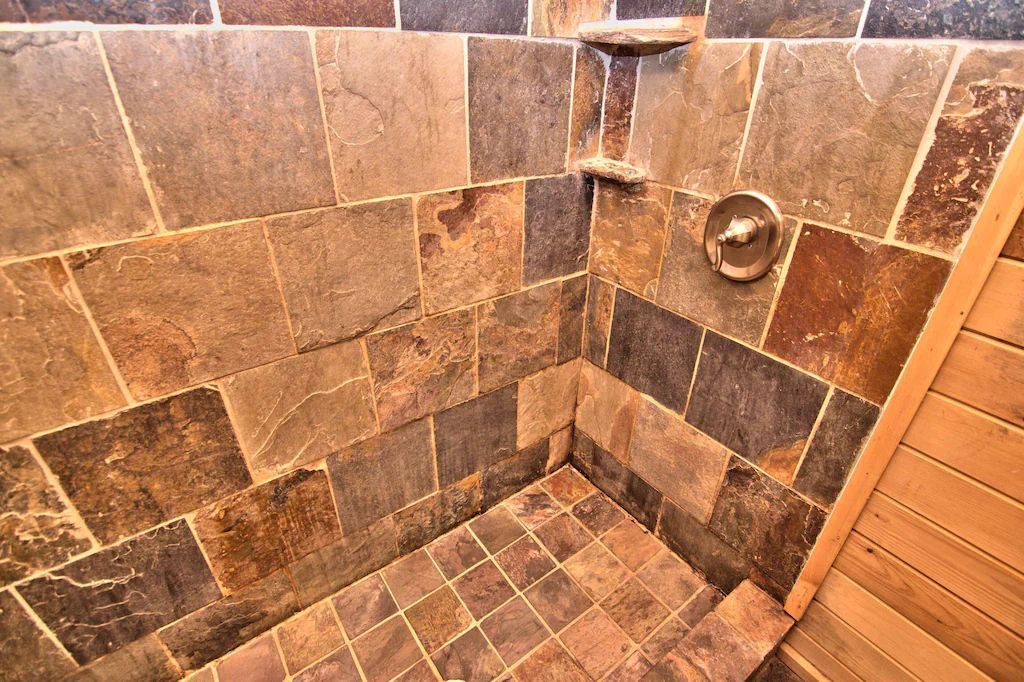 A bathroom with a tiled shower and a wooden bench.