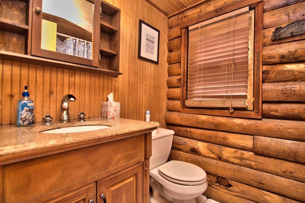 A bathroom in a log cabin with a toilet , sink , mirror and window.