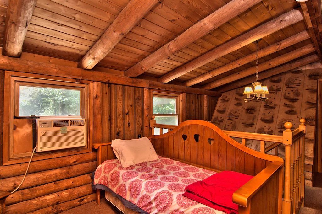 A bed in a log cabin with a window and air conditioner.