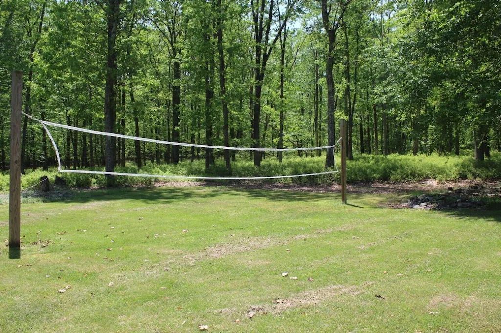 A volleyball net is in the middle of a grassy field surrounded by trees.