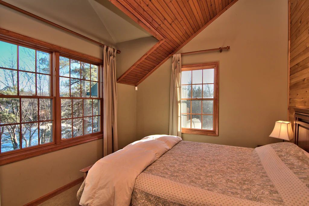 A bedroom with a bed , two windows and a wooden ceiling.