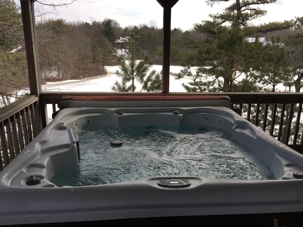 A hot tub is sitting on a deck with a view of a snowy forest.