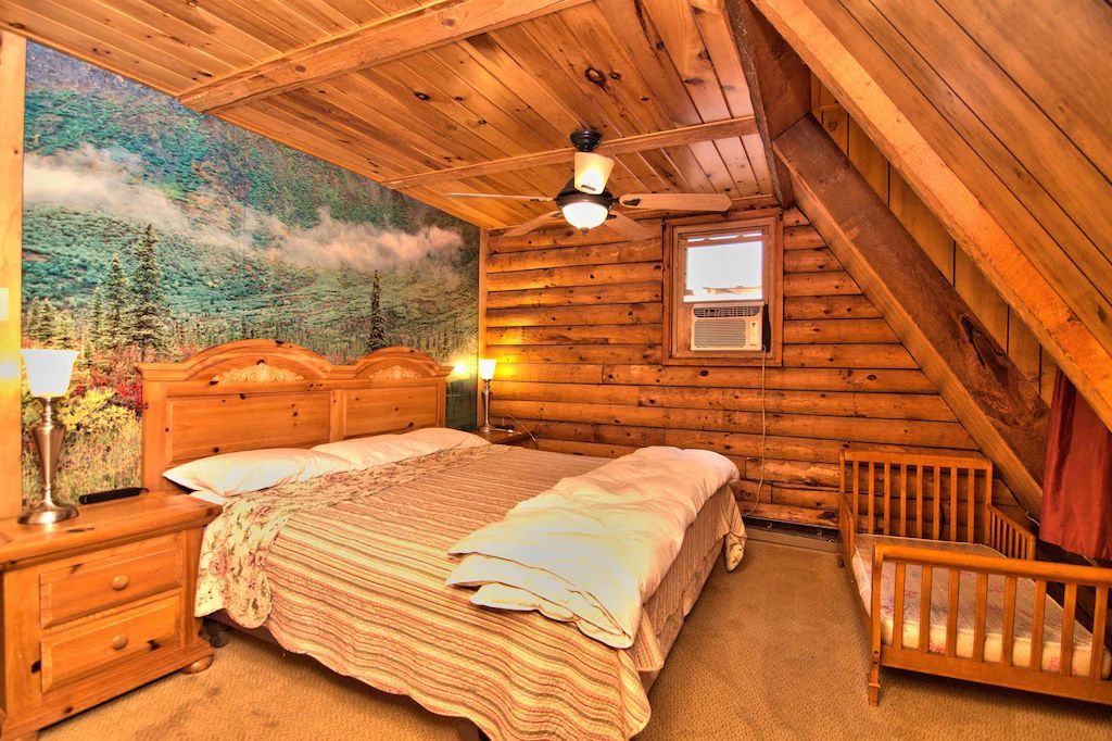 A bedroom in a log cabin with a large bed and a crib.