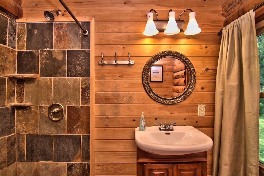 A bathroom in a log cabin with a sink , mirror and shower.