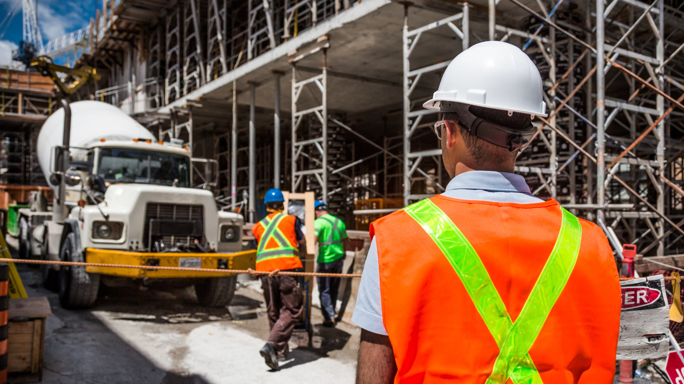 a man in an orange vest and hard hat is standing in front of a construction site .