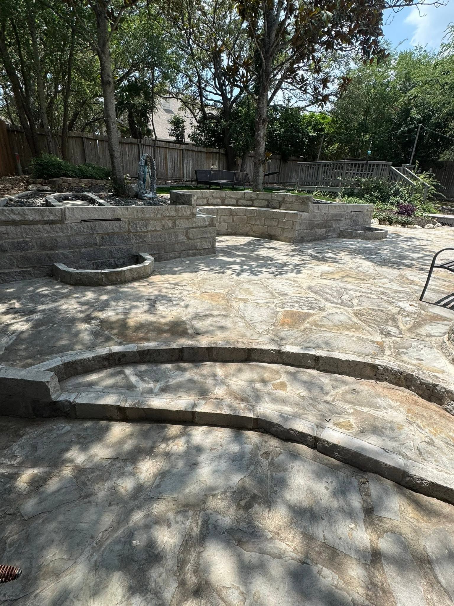 Outdoor stone amphitheater with curved seating under trees and dappled sunlight