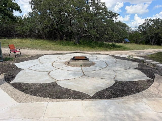 Outdoor stone fire pit with petal-shaped pattern in a park, with a red chair nearby and trees in the background