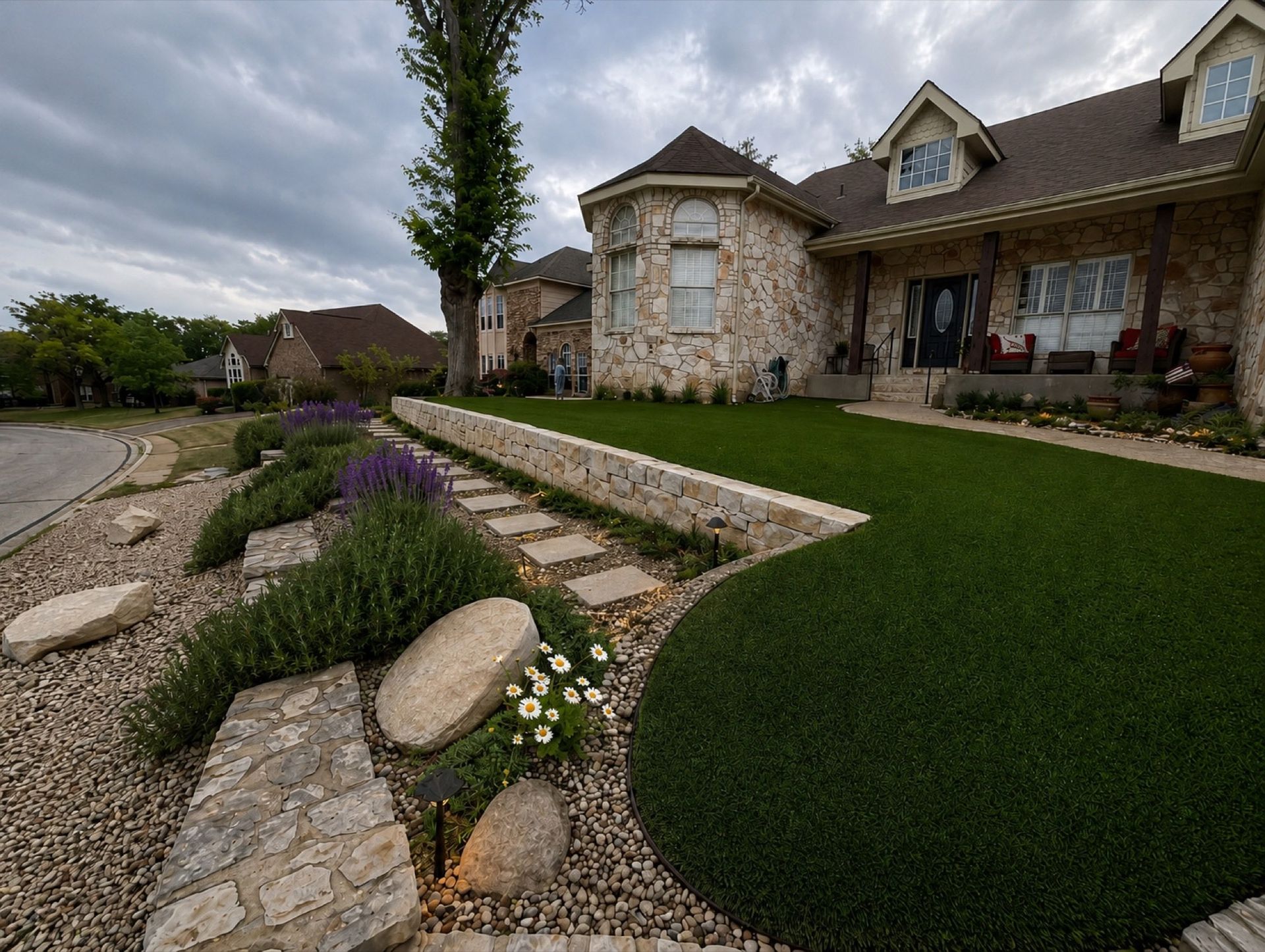 Stone walkway and landscaped front yard leading to a large suburban house under a cloudy sky