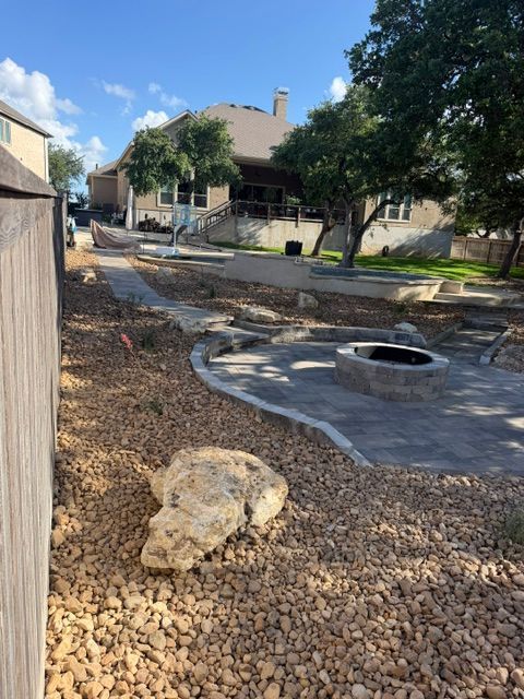 Rock garden with small stream and circular fire pit beside a suburban house