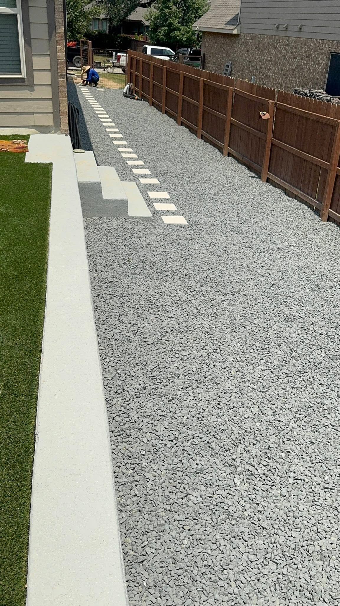 Gravel walkway beside a wooden fence and concrete stepping stones in a residential yard