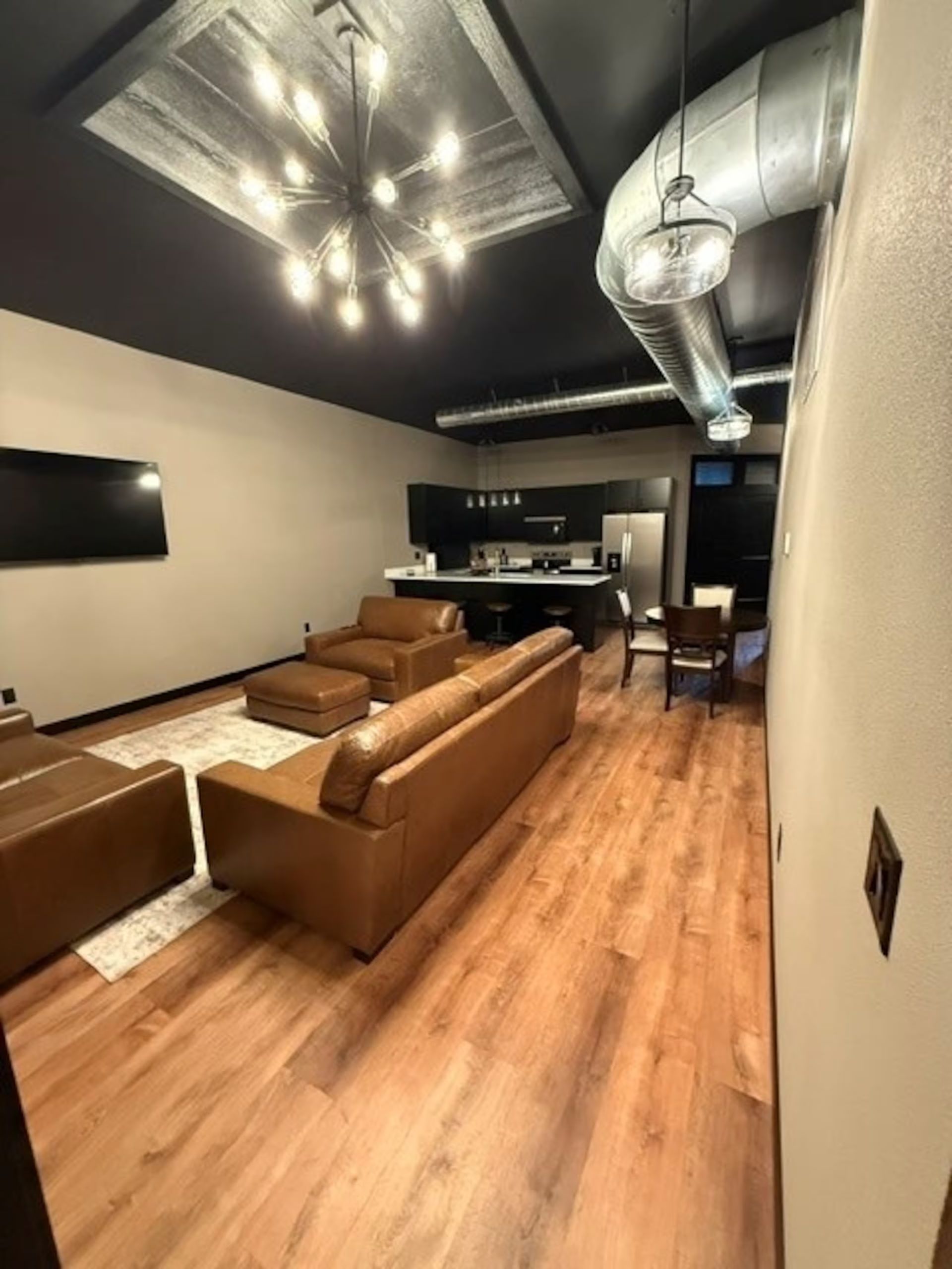 Oelwein, Iowa modern living room with brown leather sofas, wood floor, black ceiling, and exposed ductwork