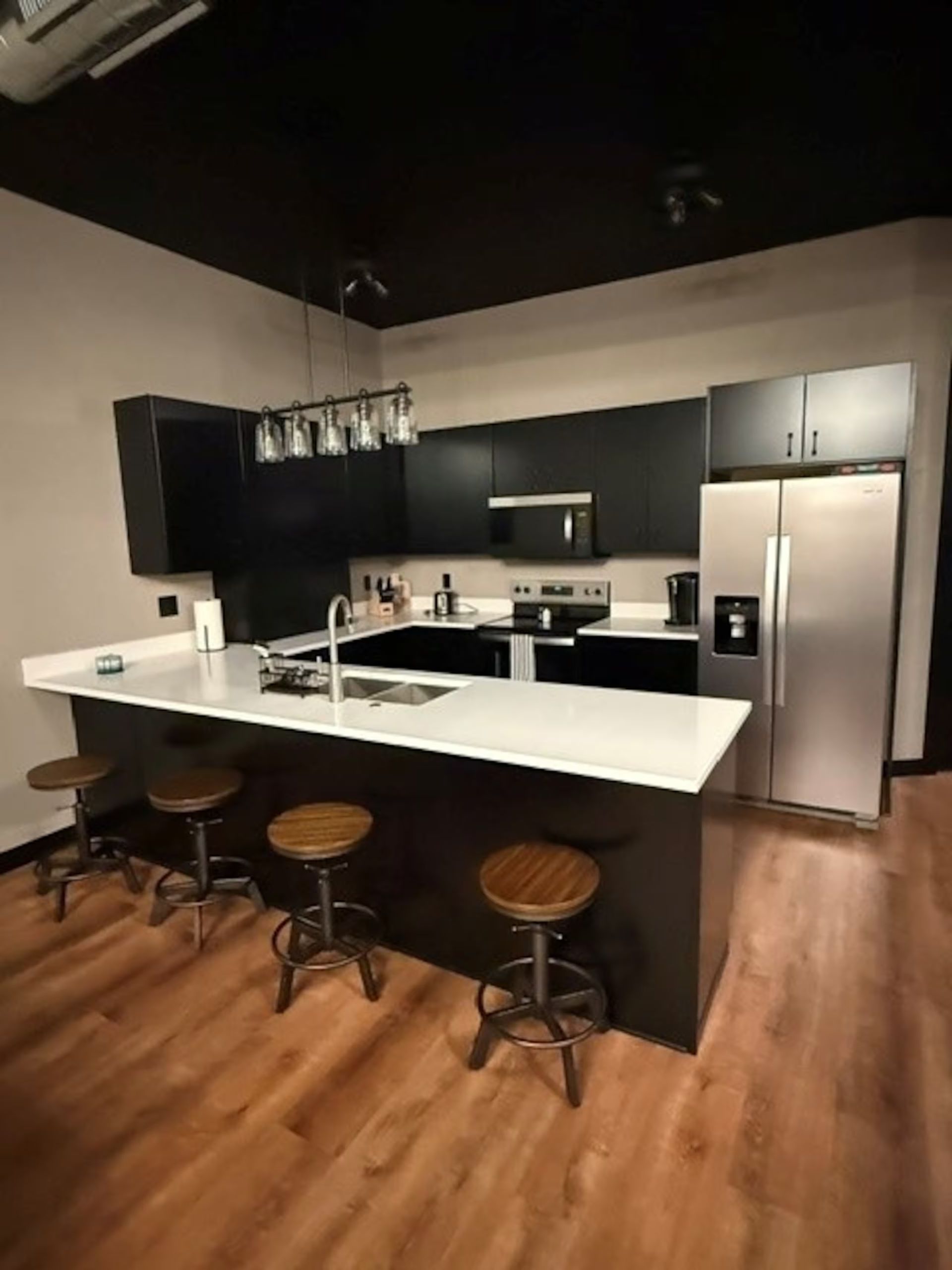 Oelwein, Iowa modern kitchen with black cabinets, white island, stainless fridge, and three stools on wood flooring