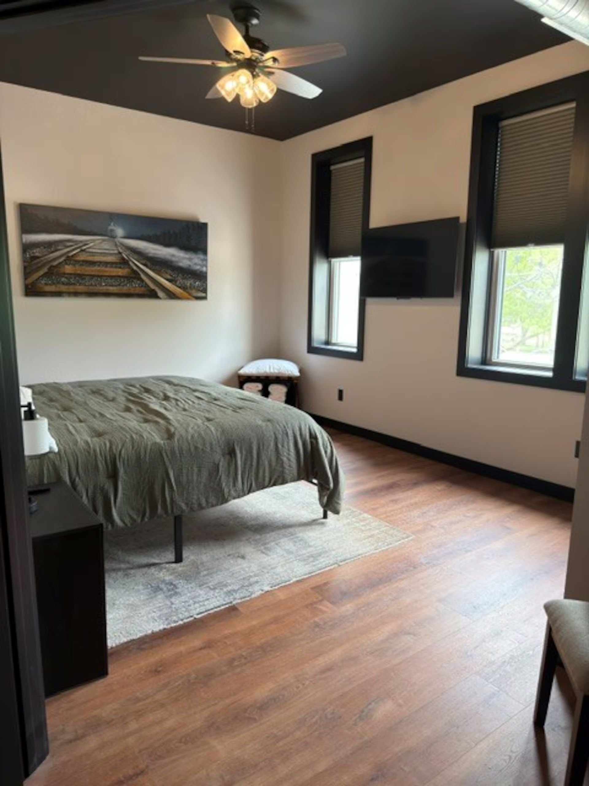 Oelwein, Iowa modern bedroom with a bed, ceiling fan, dark trim, and two windows with blinds.