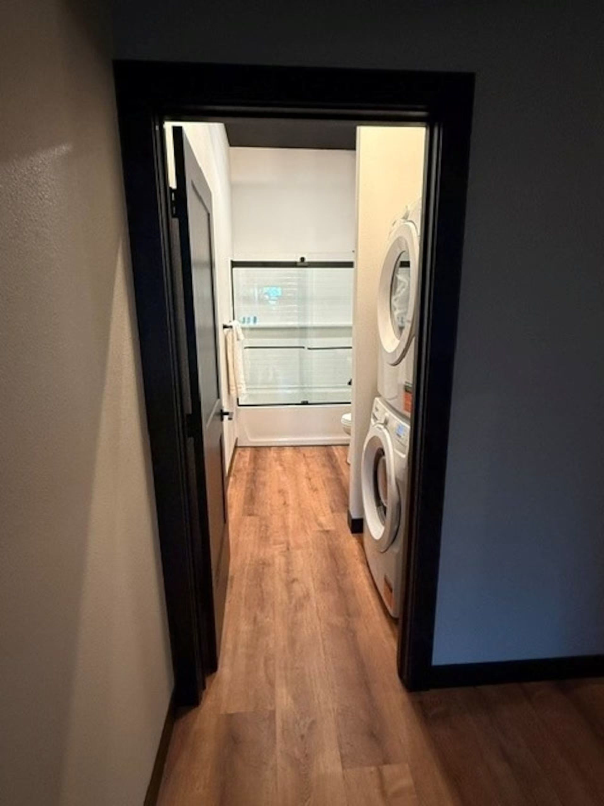 Oelwein, Iowa laundry closet with stacked washer and dryer, white shelving, and wood flooring behind a doorway