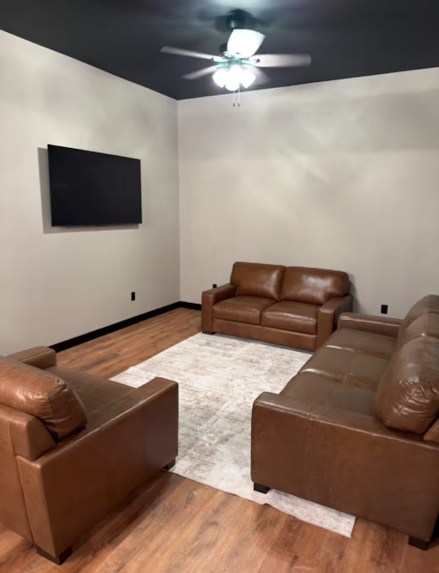 Oelwein, Iowa living room with brown leather sofas, wall-mounted TV, white rug, and ceiling fan with light.