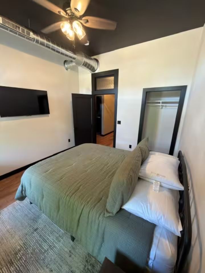 Oelwein, Iowa modern bedroom with green bedding, wall-mounted TV, ceiling fan, and open doorway
