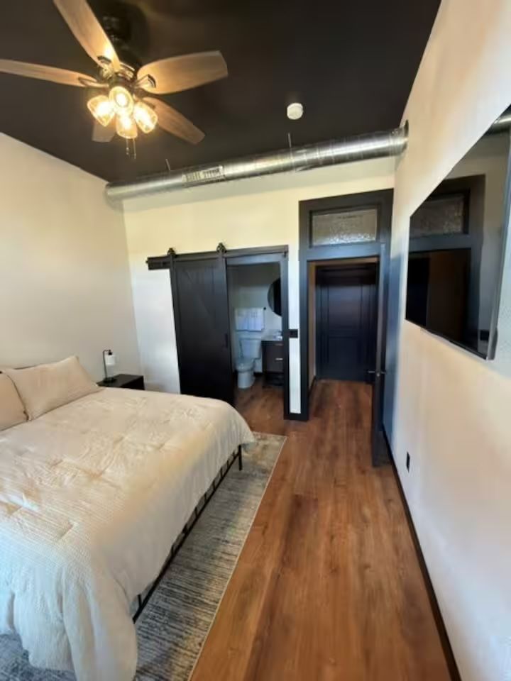 Oelwein, Iowa bedroom with white bedding, dark closet doors, and wood flooring with a ceiling fan.