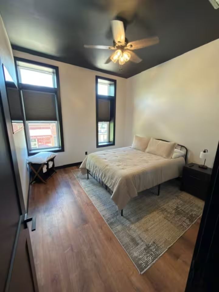 Oelwein, Iowa bright bedroom with a bed, two windows, ceiling fan, wood floor, and neutral decor