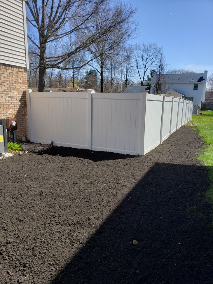 White vinyl fence bordering a backyard with fresh mulch, next to a brick building.