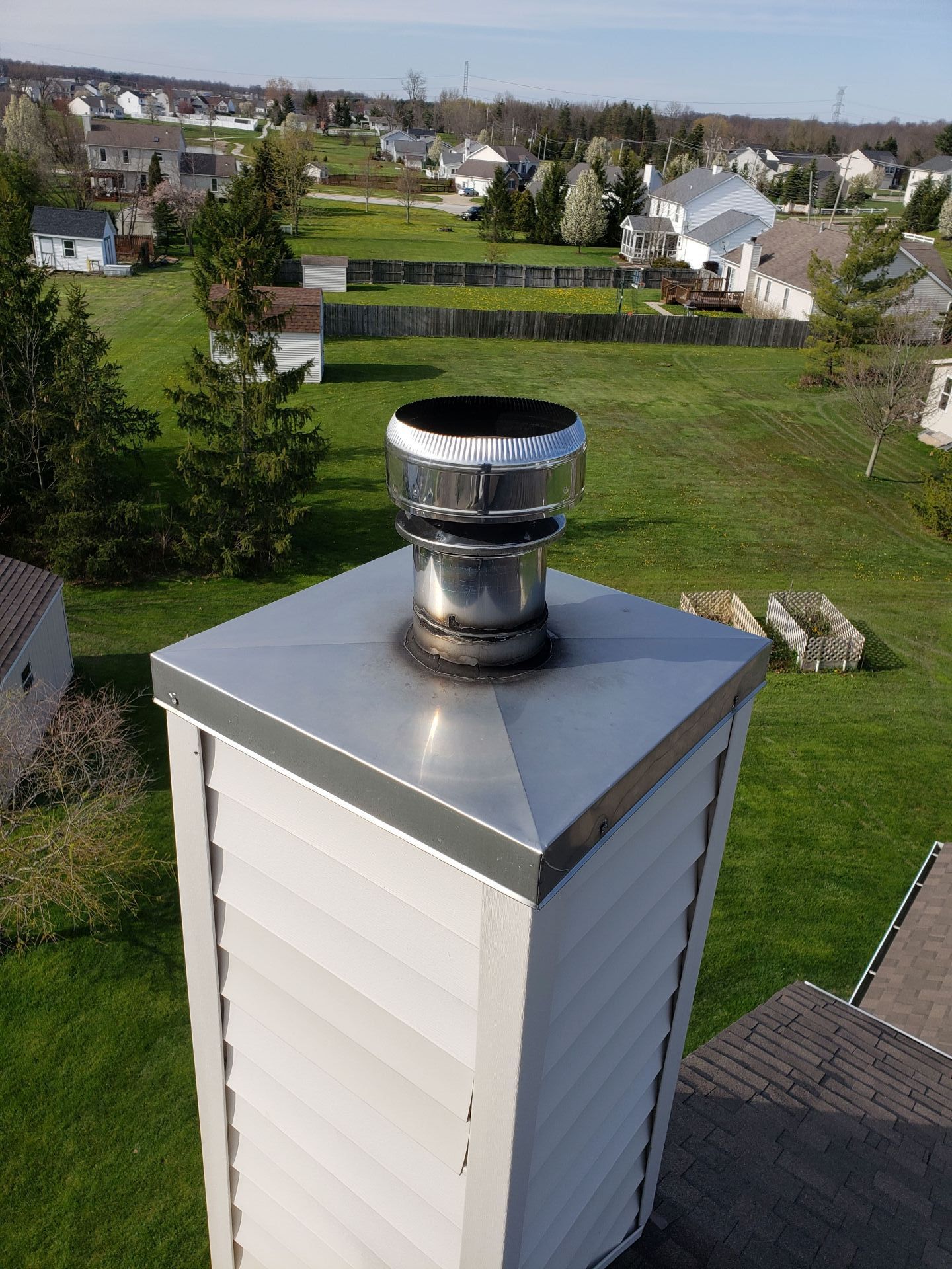 Chimney on a roof with a metal cap and spark arrester; residential neighborhood in the background.