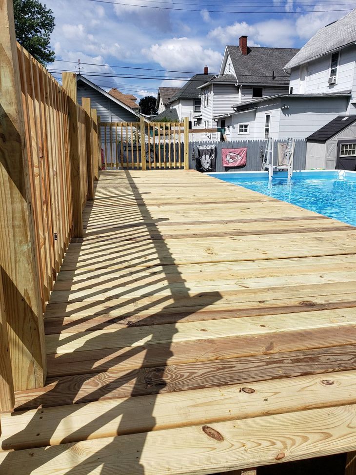Wooden pool deck with fence and gate, leading to a blue swimming pool in a residential area.