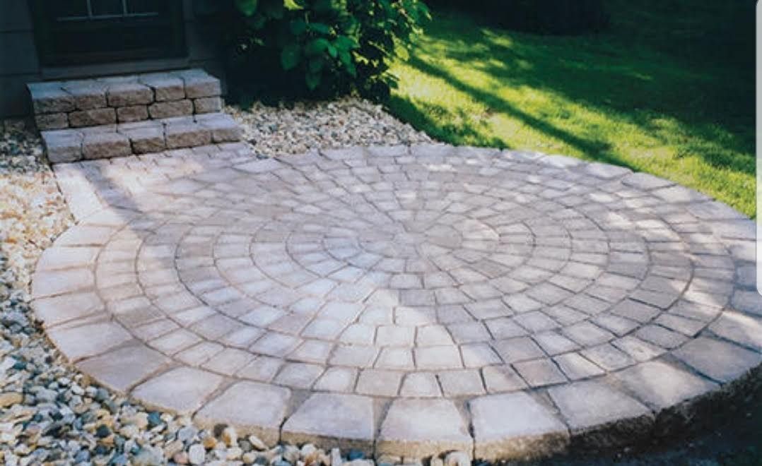 Circular paved patio with brick steps, set in a yard with gravel and grass.