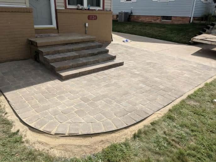 Brick patio with steps leading to a house entrance. Green grass surrounds the patio.