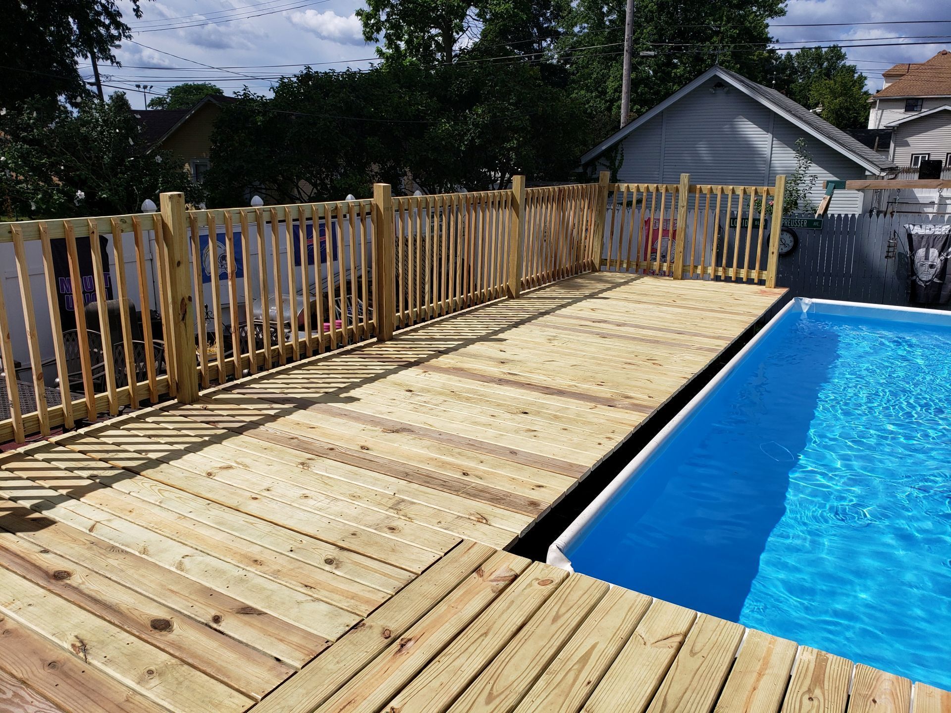 Wooden pool deck with blue water. Fence surrounds deck and pool.