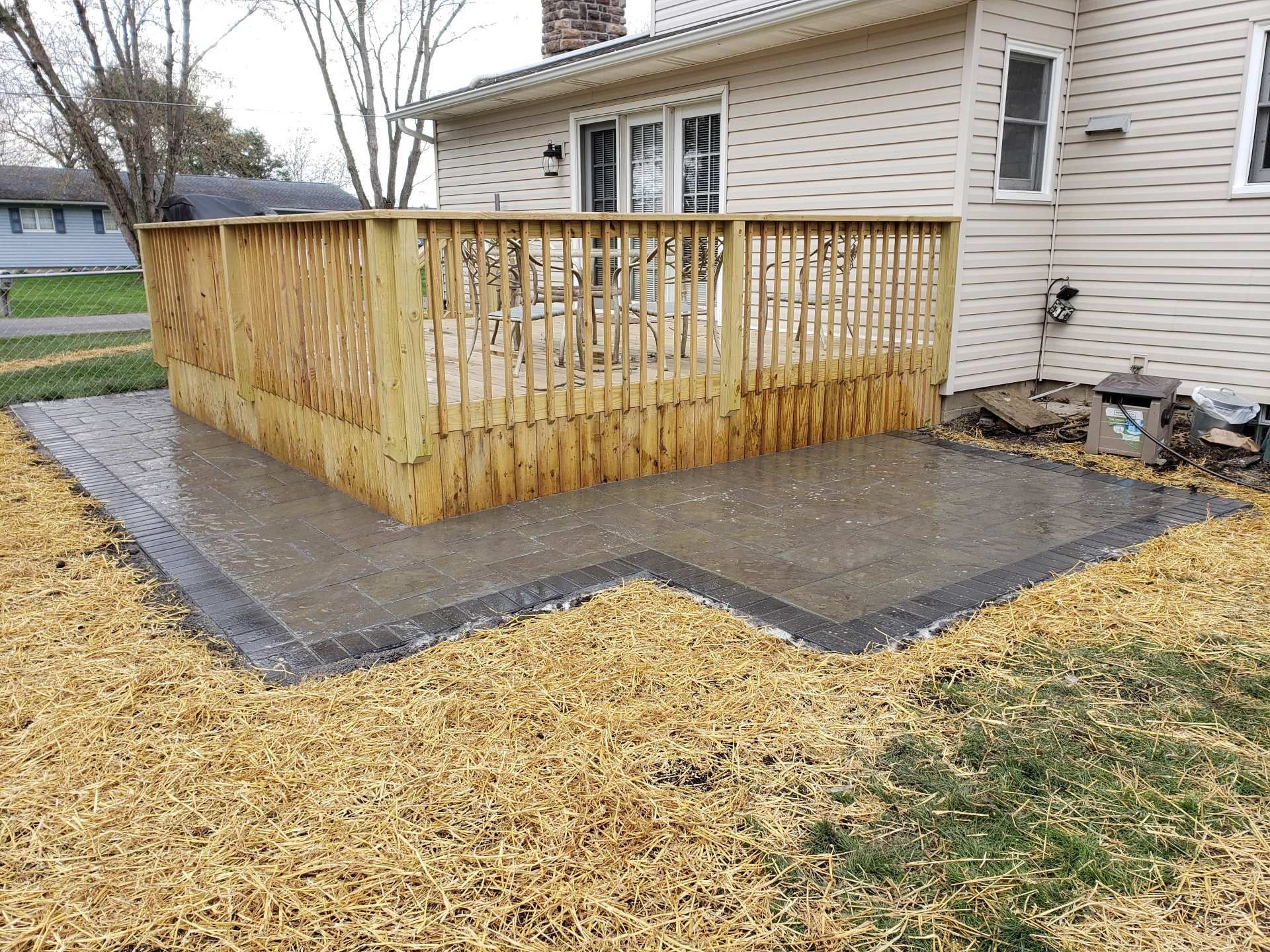 Concrete patio with wooden deck, surrounded by dry grass, next to a house.
