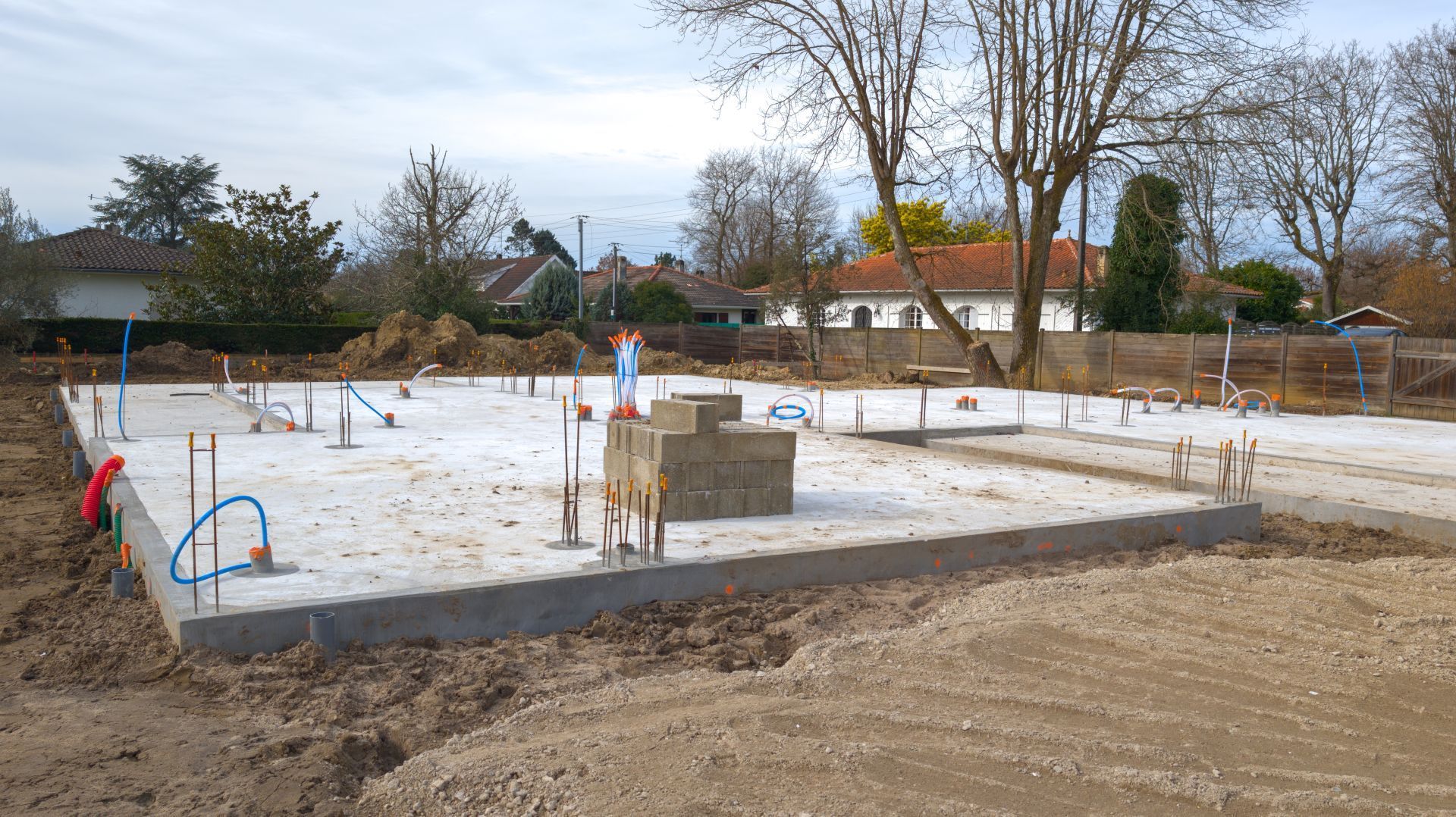 Concrete foundation for a building under construction, with pipes and rebar visible; dirt surrounding it.