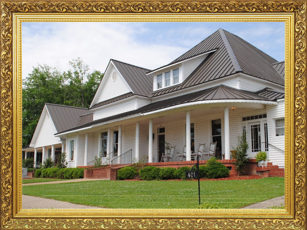 Large white house with a gray roof, front porch, and manicured lawn framed by a gold border