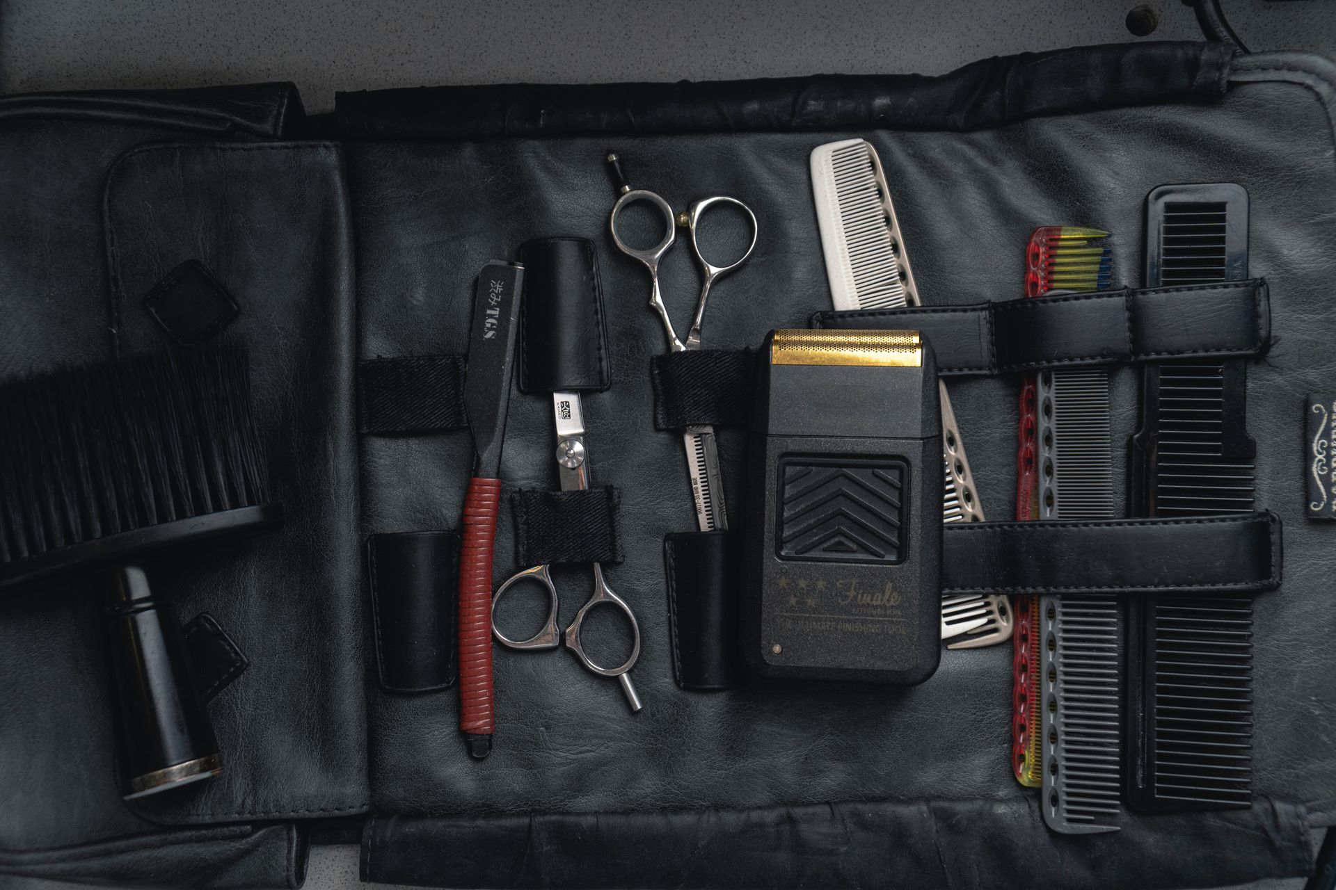 Black leather barber tool kit with scissors, combs, and a razor.