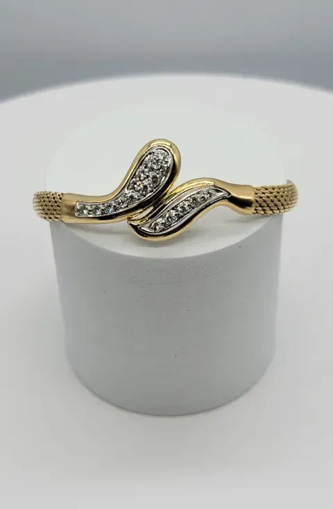 Gold bracelet with black-and-clear jeweled wave design on a white display stand